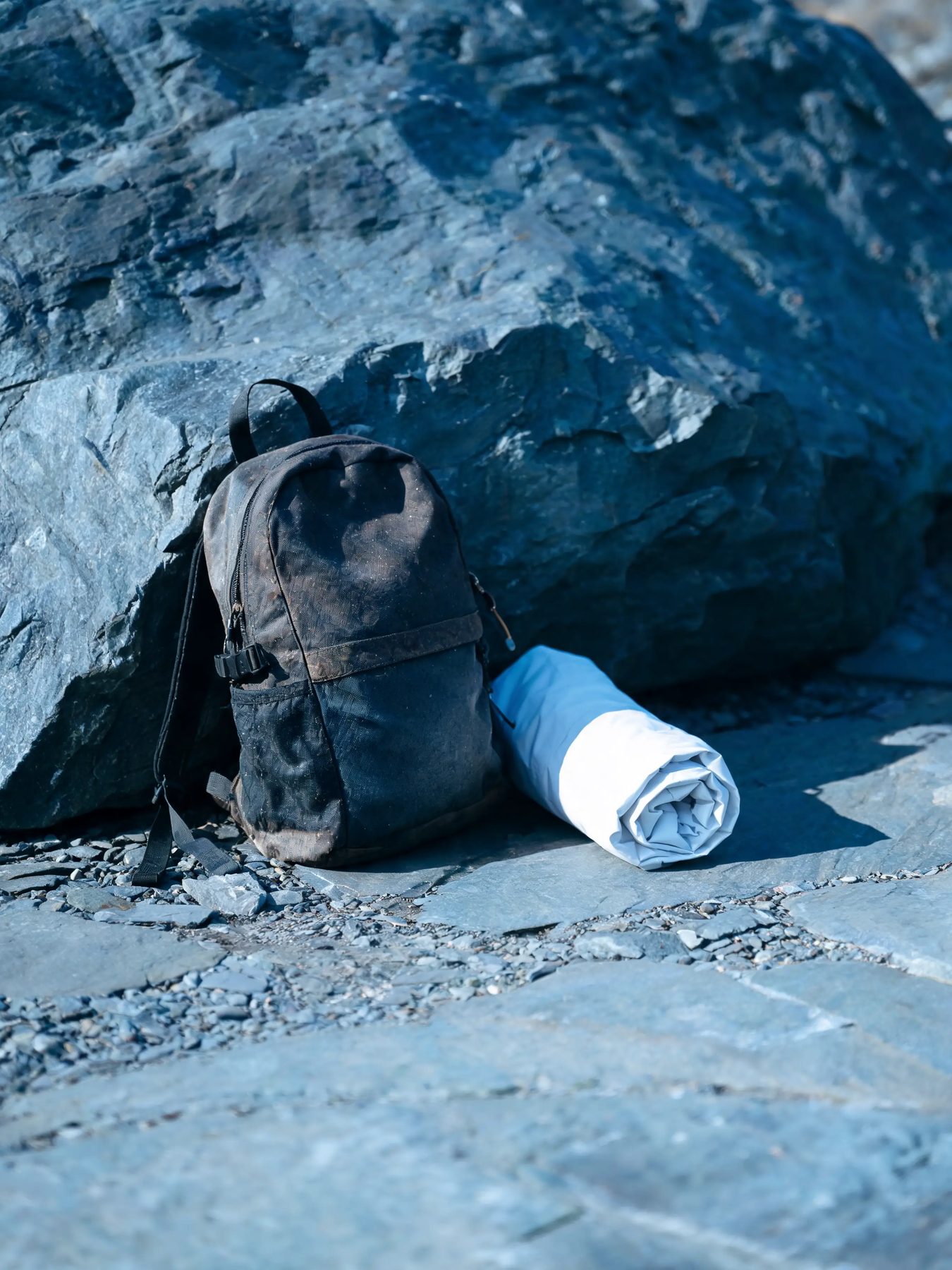 Ripstop daypack and rolled shell jacket against a slate boulder